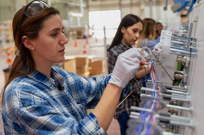 Kadın teknisyen, elektrik panosunda kablo bağlantıları yapıyor, iş ortamında dikkatli çalışıyor.