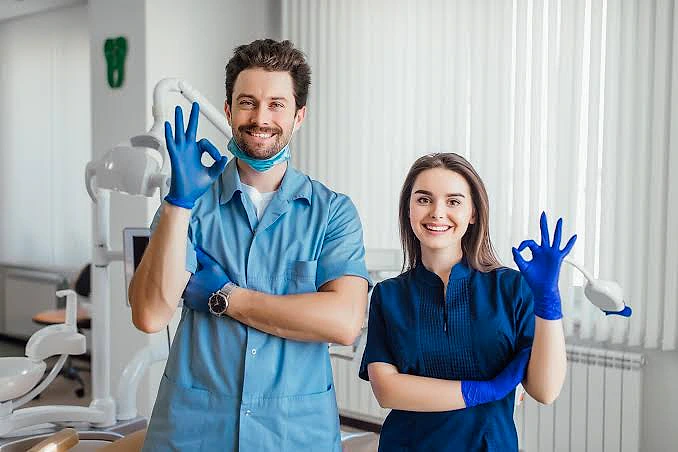 Diş hekimleri, diş kliniğinde poz veren iki genç uzman, başarı işareti yapıyor.