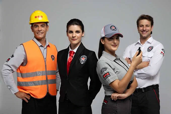 Farklı güvenlik görevlisi kıyafetleri giymiş dört kişi, profesyonel bir ortamda duruyor.